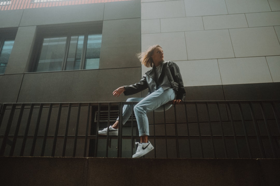 woman in black jacket and blue denim jeans sitting on black metal railings