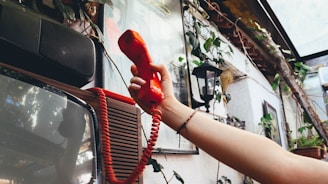 person holding red telephone near white car