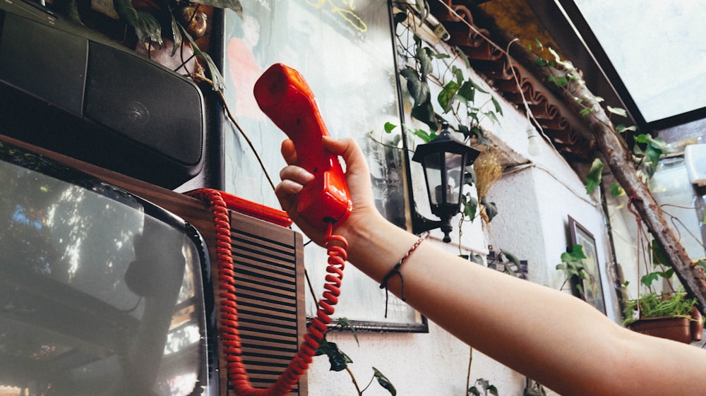 person holding red telephone near white car