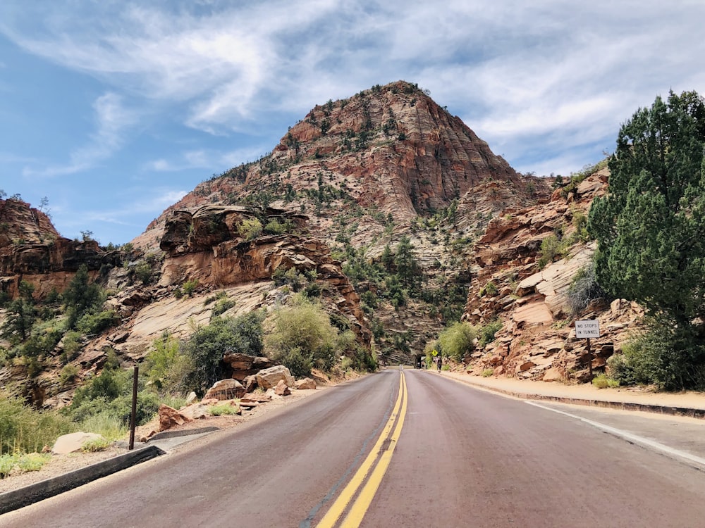 gray asphalt road near brown rock mountain under blue sky during daytime