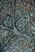 A close-up of an abstract textured surface featuring irregular patterns resembling neural networks or biological structures. The surface appears metallic with reflective qualities and intricate grooves.