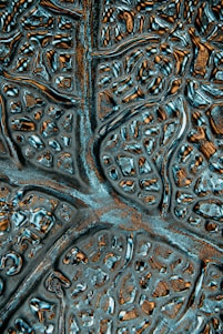A close-up of an abstract textured surface featuring irregular patterns resembling neural networks or biological structures. The surface appears metallic with reflective qualities and intricate grooves.