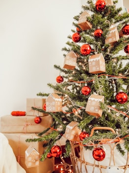 festive picture of red globe ornaments and ginger bread house ornaments on green chistmas pine tree