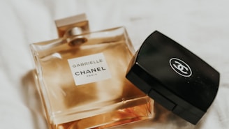 A classy and elegant display of a Chanel perfume bottle alongside a black compact case. The light reflects softly off their surfaces, creating a luxurious ambiance.