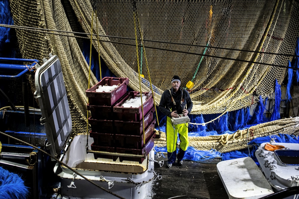 man in black jacket and green pants standing beside red and black plastic crate