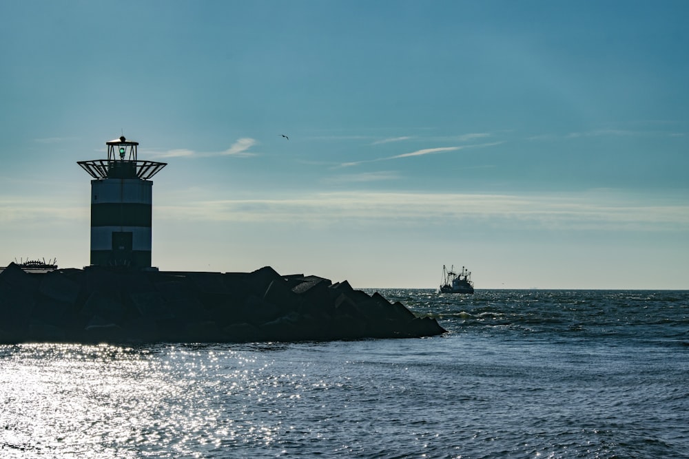 silhouette of lighthouse on rock formation near body of water during daytime