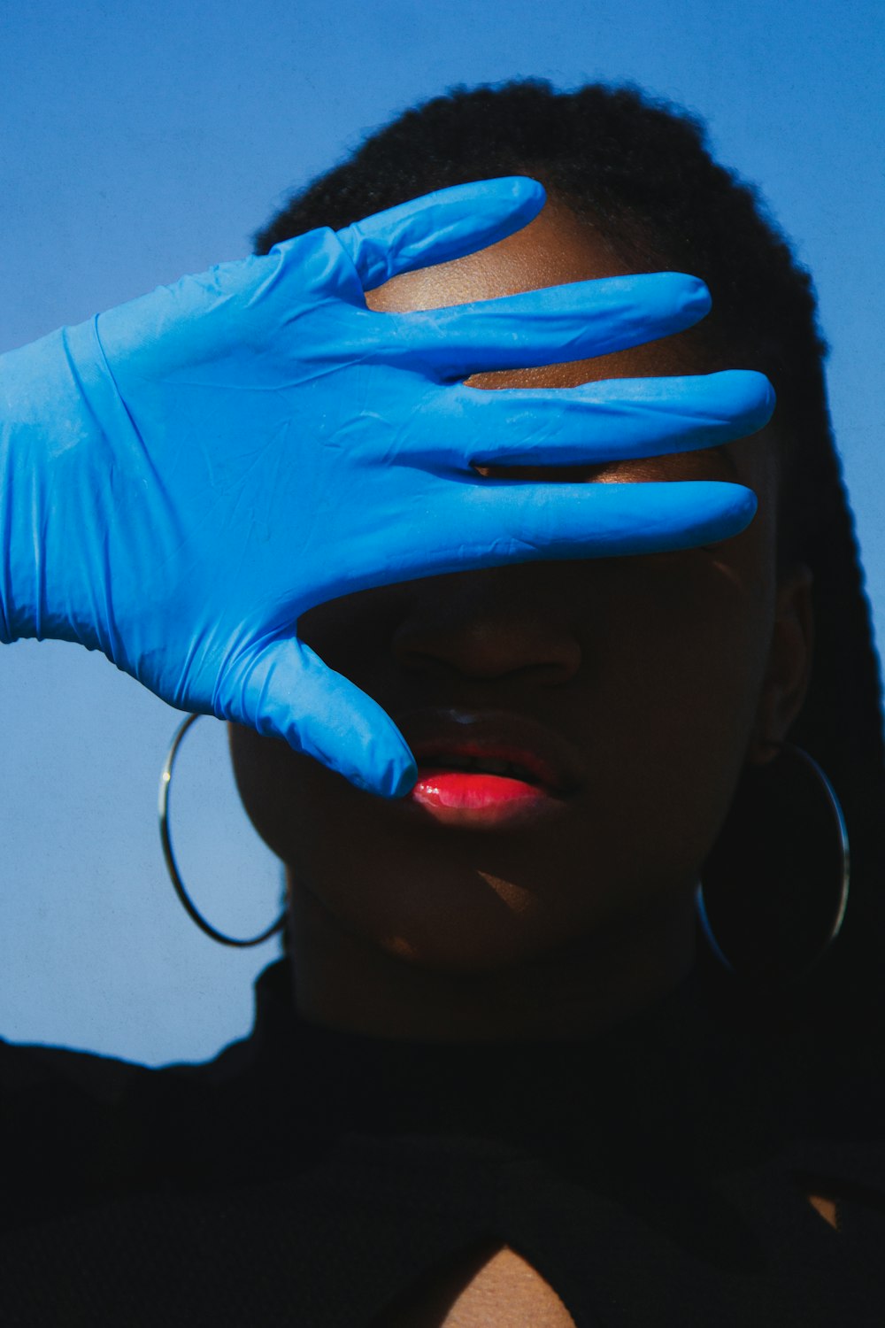 Frau verbirgt ihr Gesicht teilweise mit einem blauen medizinischen Latexhandschuh