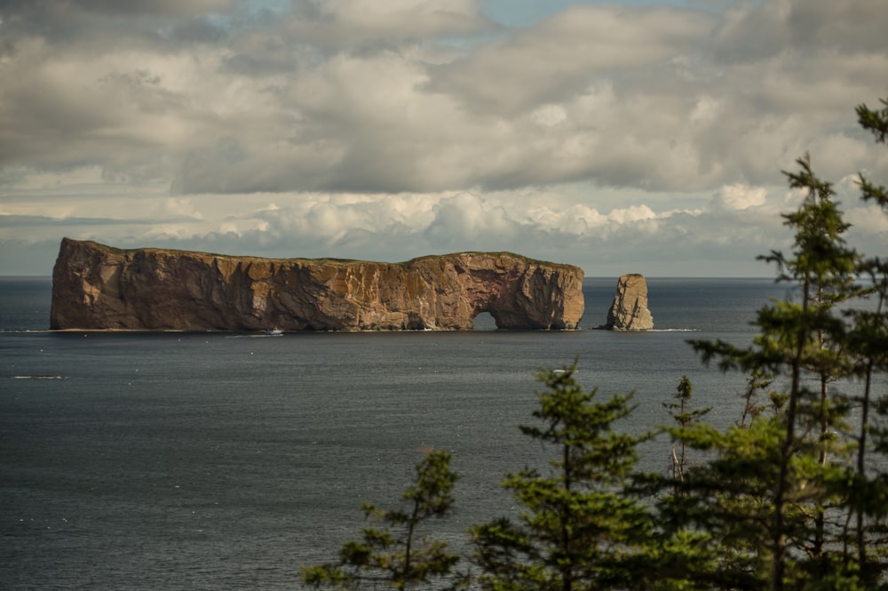 brown rock formation near body of water under cloudy sky during daytime