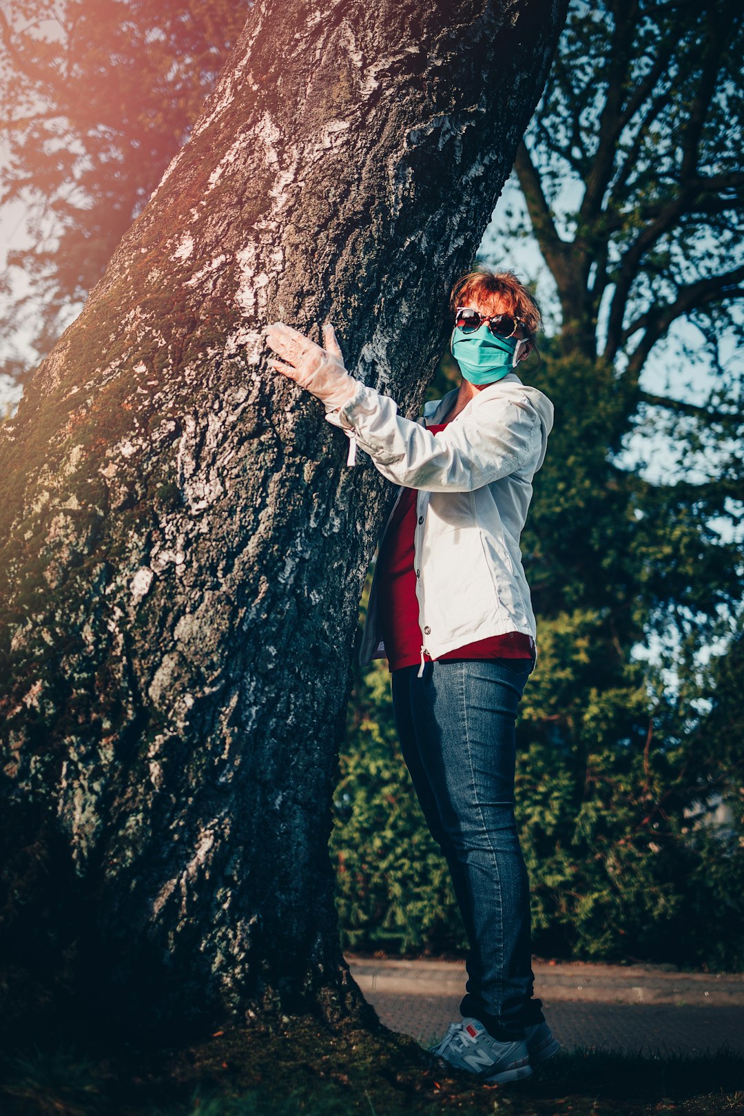 woman in white jacket and blue denim jeans standing beside brown tree during daytime