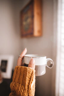 A vibrant hand-thrown ceramic mug in sunny yellow with a cozy knitted sleeve beside a steaming cup of tea.