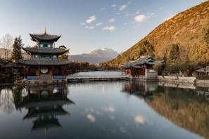 brown and green pagoda on body of water near mountain under blue sky during daytime