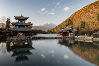 brown and green pagoda on body of water near mountain under blue sky during daytime