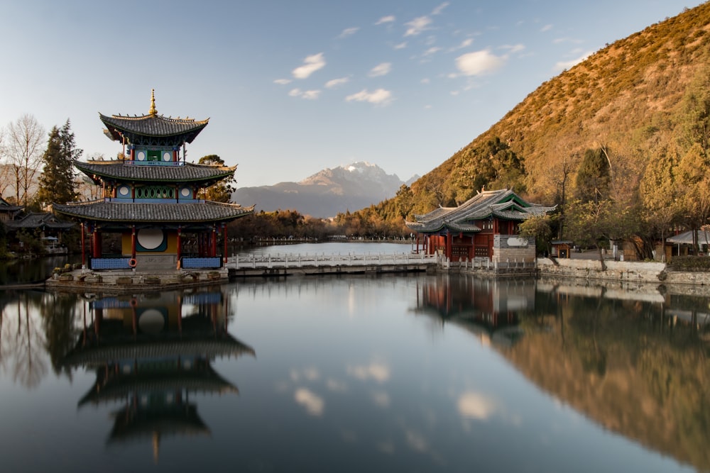 brown and green pagoda on body of water near mountain under blue sky during daytime