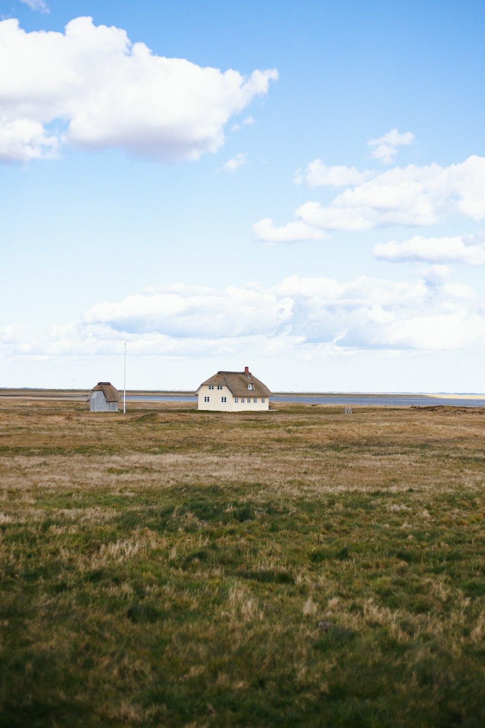 Weißes und braunes Haus auf grünem Rasenfeld unter weißen Wolken tagsüber