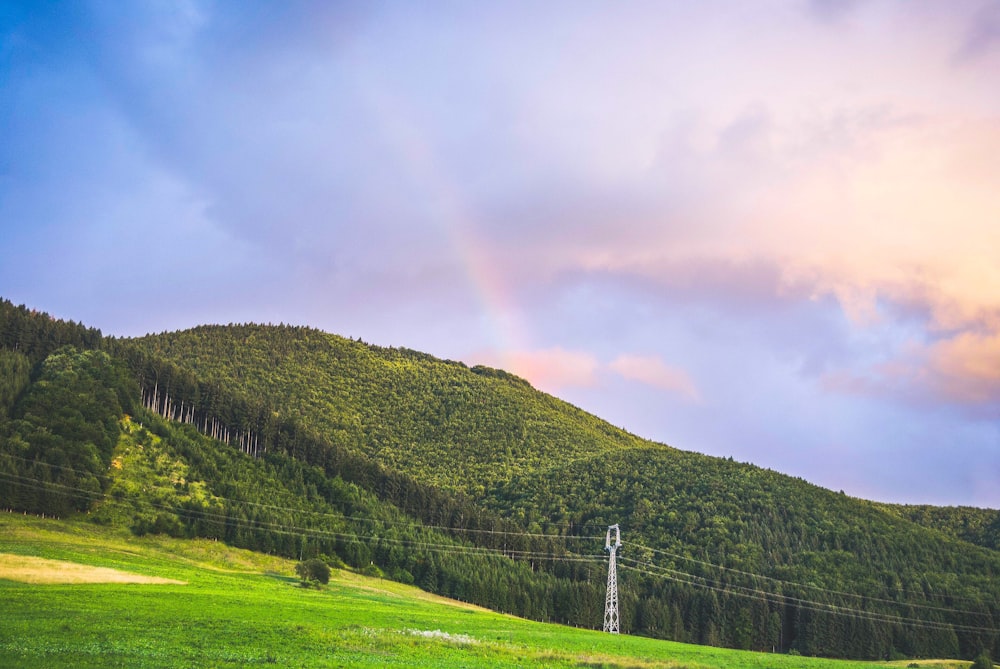 green grass field and mountain under white clouds and rainbow