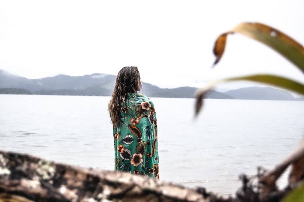 woman in green and white floral dress standing on rock near body of water during daytime