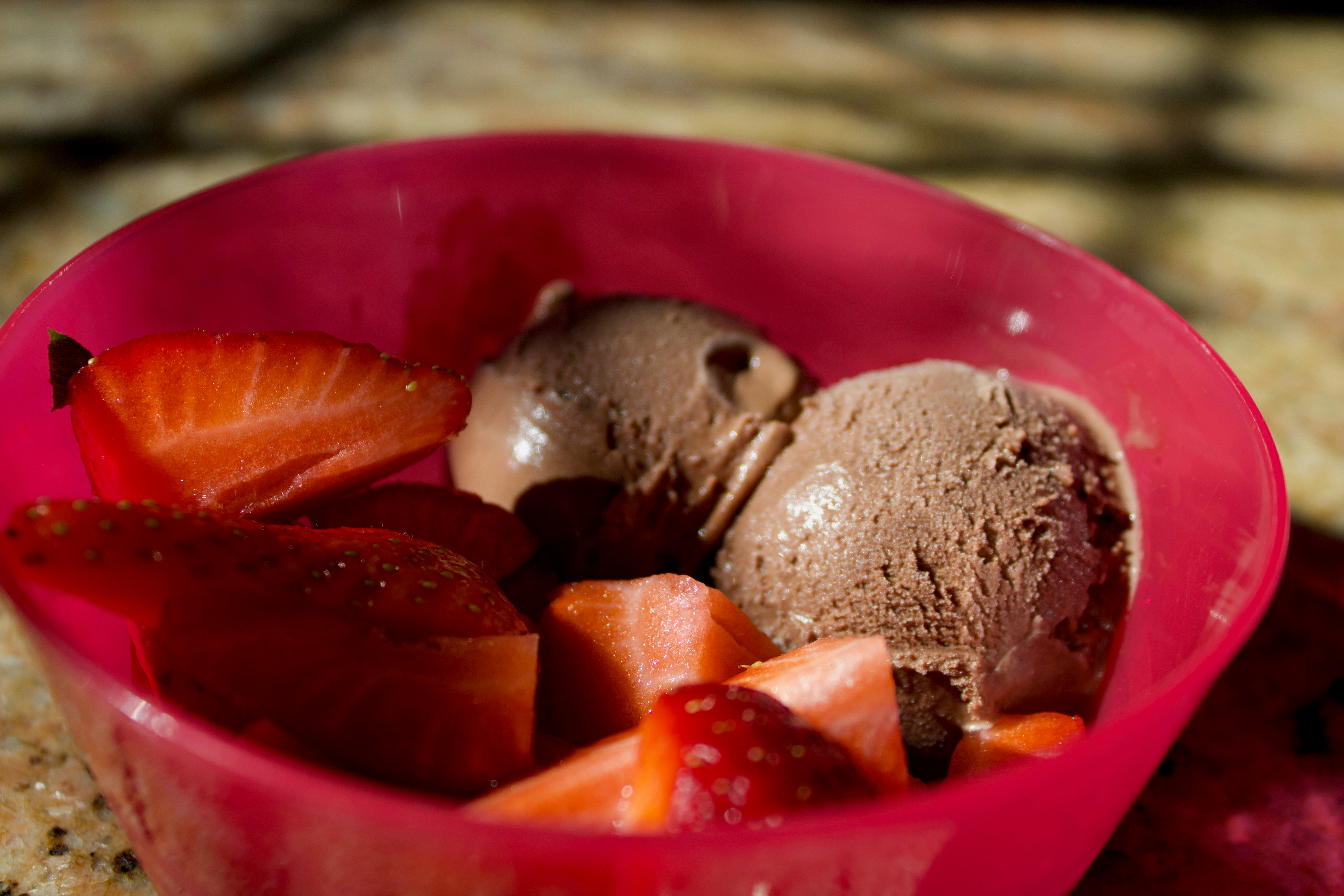Pink strawberry ice cream scoop in a cone with fresh strawberry garnish, bright background