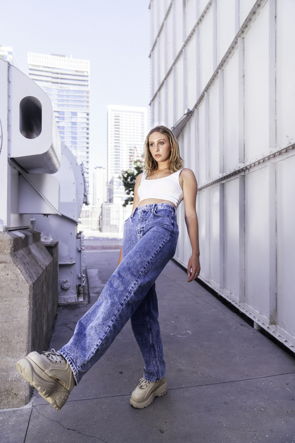 Mujer en jeans de mezclilla azul de pie sobre piso de concreto gris durante el día