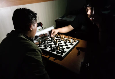 A focused chess coach guiding a young student through a strategic move in a warmly lit room with deep crimson and forest green accents.