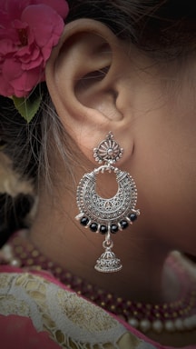 An intricately designed silver earring with black beads complements a traditional attire. A red floral hair accessory adds a touch of elegance, with fine detailing visible on both the earring and the fabric.