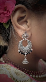 An intricately designed silver earring with black beads complements a traditional attire. A red floral hair accessory adds a touch of elegance, with fine detailing visible on both the earring and the fabric.