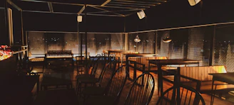 Outdoor terrace with wooden tables surrounded by greenery and soft evening lights.