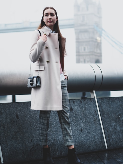 A stylish model wearing a sleek, tailored luxury coat standing against a city backdrop