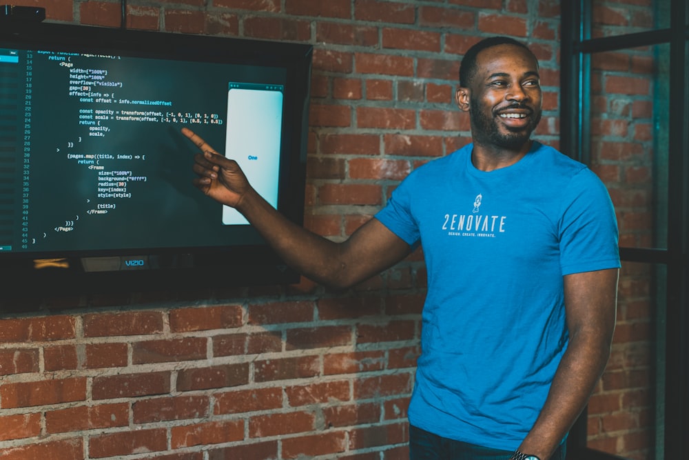 man in blue crew neck t-shirt standing beside brown brick wall