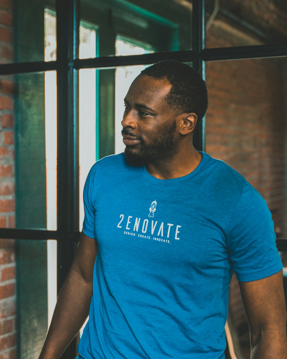 man in blue crew neck t-shirt standing near brown wooden wall