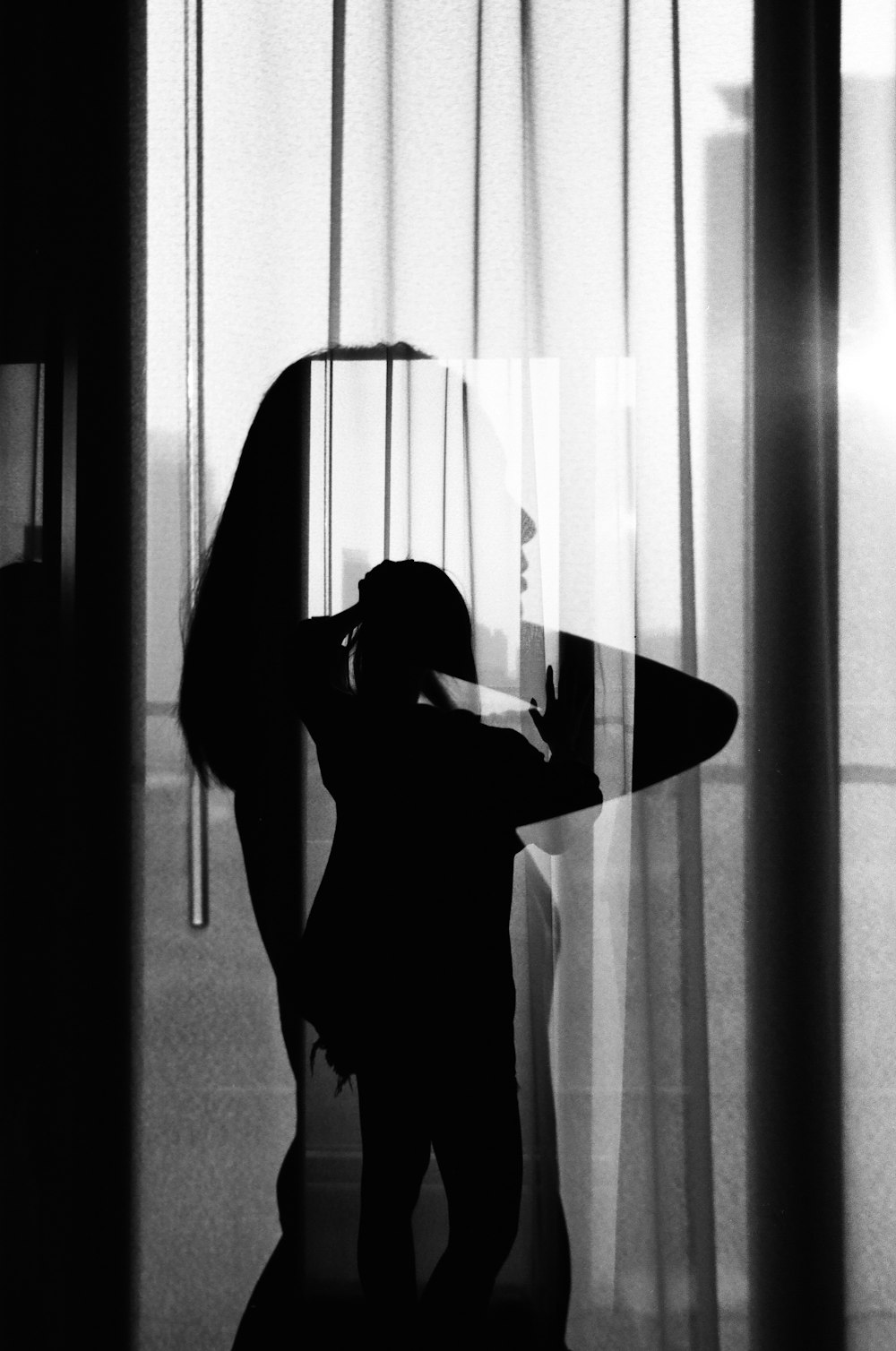 窓のカーテンの前に立つ黒いタンクトップの女性
