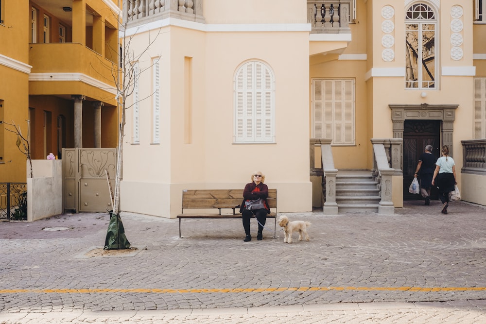 man in blue jacket sitting on bench beside white dog during daytime