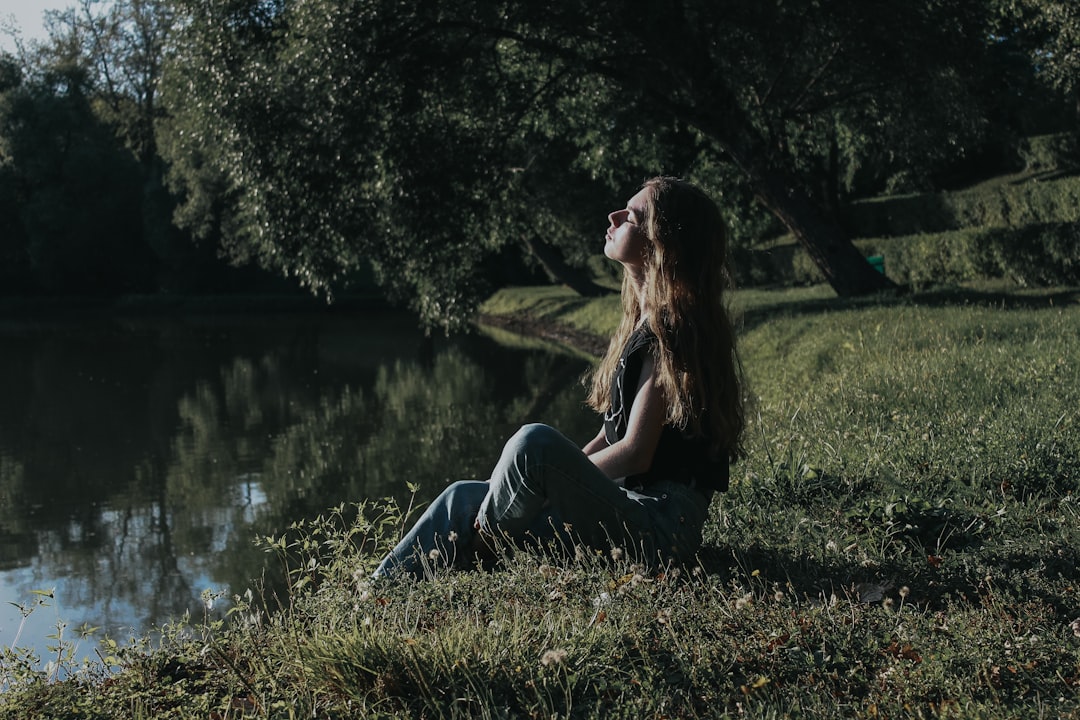 woman in gray tank top and blue denim jeans sitting on green grass field during daytime