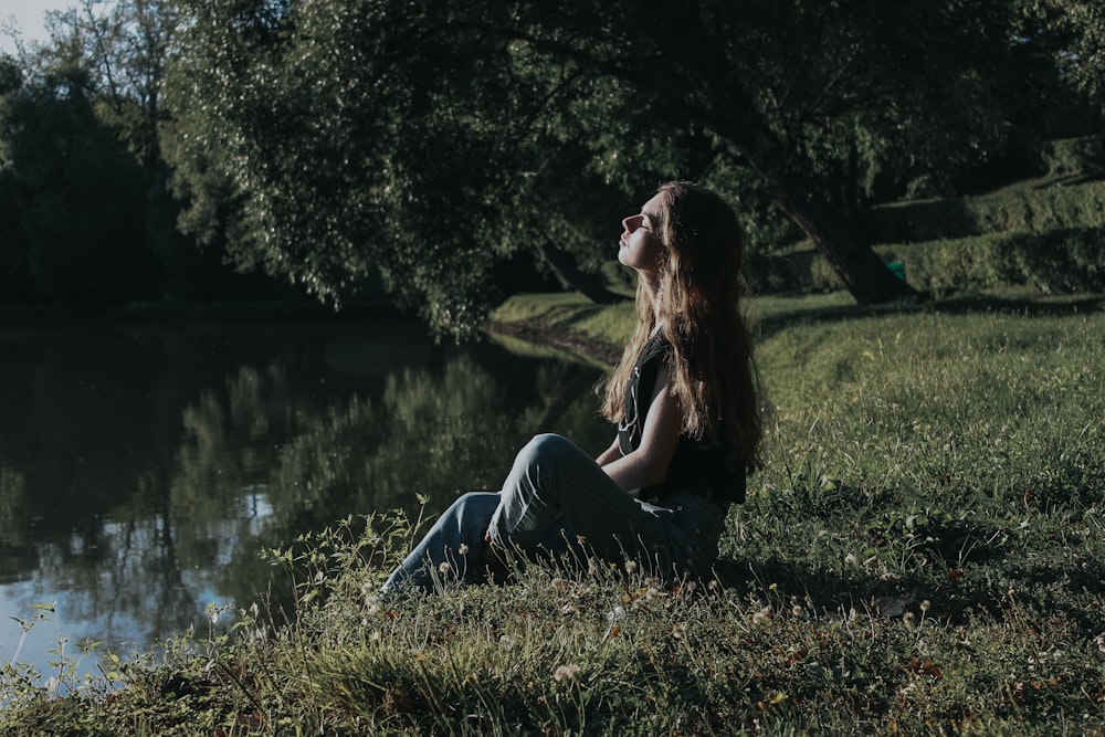 woman in gray tank top and blue denim jeans sitting on green grass field during daytime