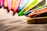 Multiple colorful wax crayons are lined up at the edge of a textured surface, displaying a variety of vibrant hues. The light highlights the texture and color details of the crayons, creating a vivid and artistic composition.