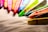 Multiple colorful wax crayons are lined up at the edge of a textured surface, displaying a variety of vibrant hues. The light highlights the texture and color details of the crayons, creating a vivid and artistic composition.