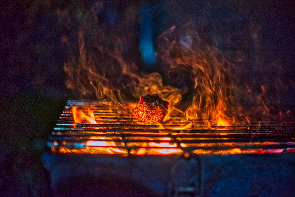 Flames rising around meat cooking on a live-fire grill