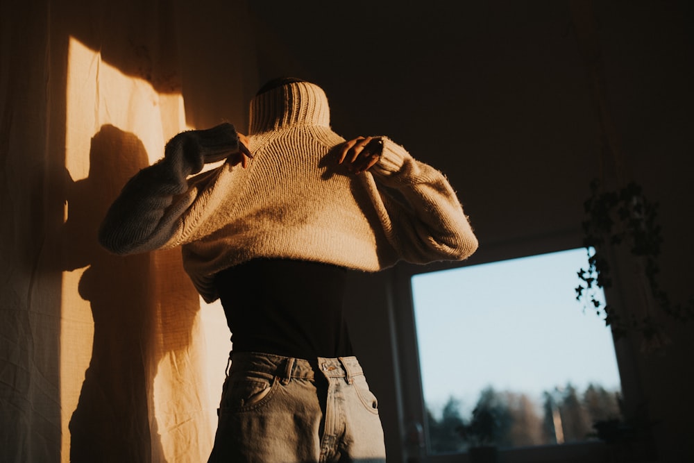 person in white knit sweater and gray denim jeans standing near window during daytime