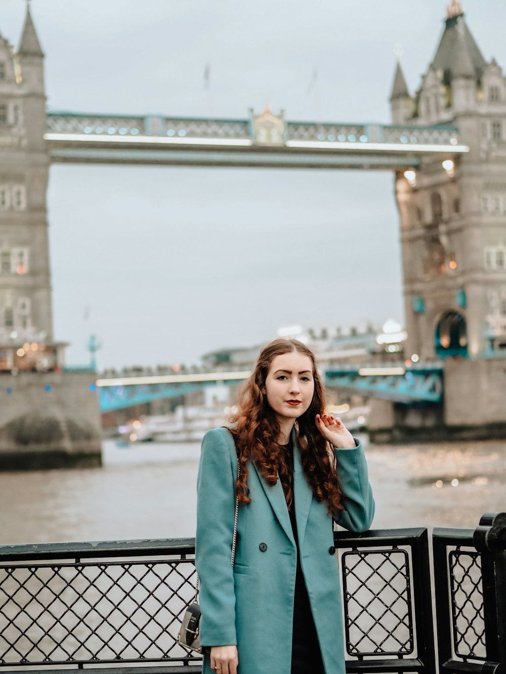 woman in blue coat standing near bridge during daytime