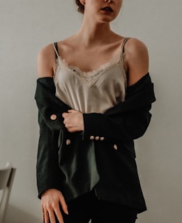 A close-up shot of a model wearing a sleek, cream-colored blouse paired with tailored charcoal trousers, standing against a softly lit urban backdrop.