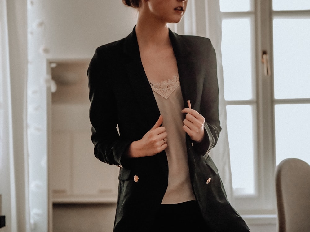 femme en blazer noir debout près du mur blanc