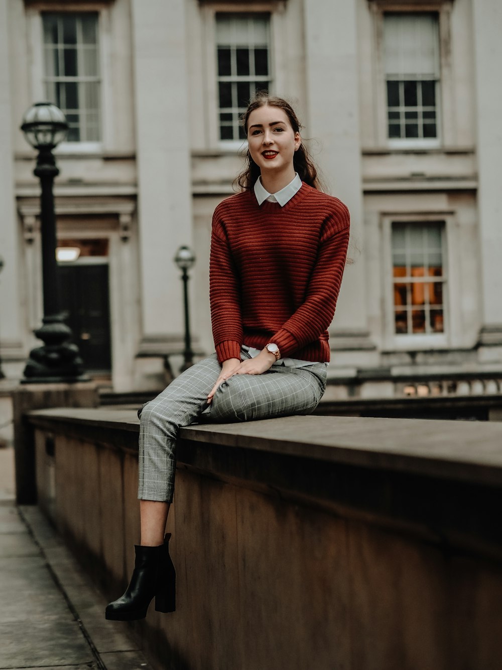 donna in maglione rosso e jeans blu denim seduta su una panca di legno marrone durante il giorno