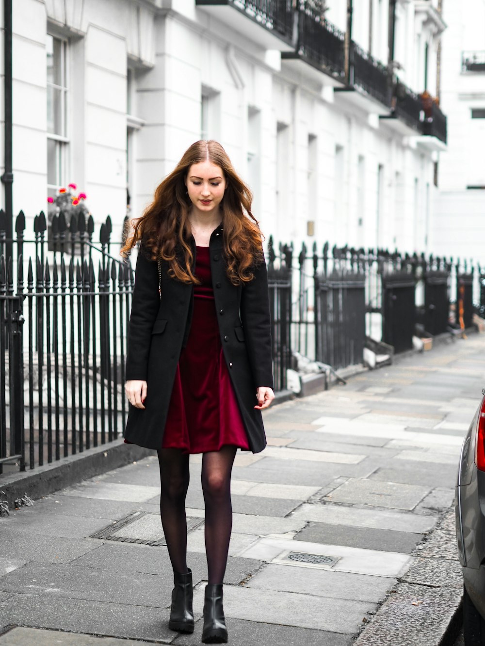 woman in black coat standing on sidewalk during daytime