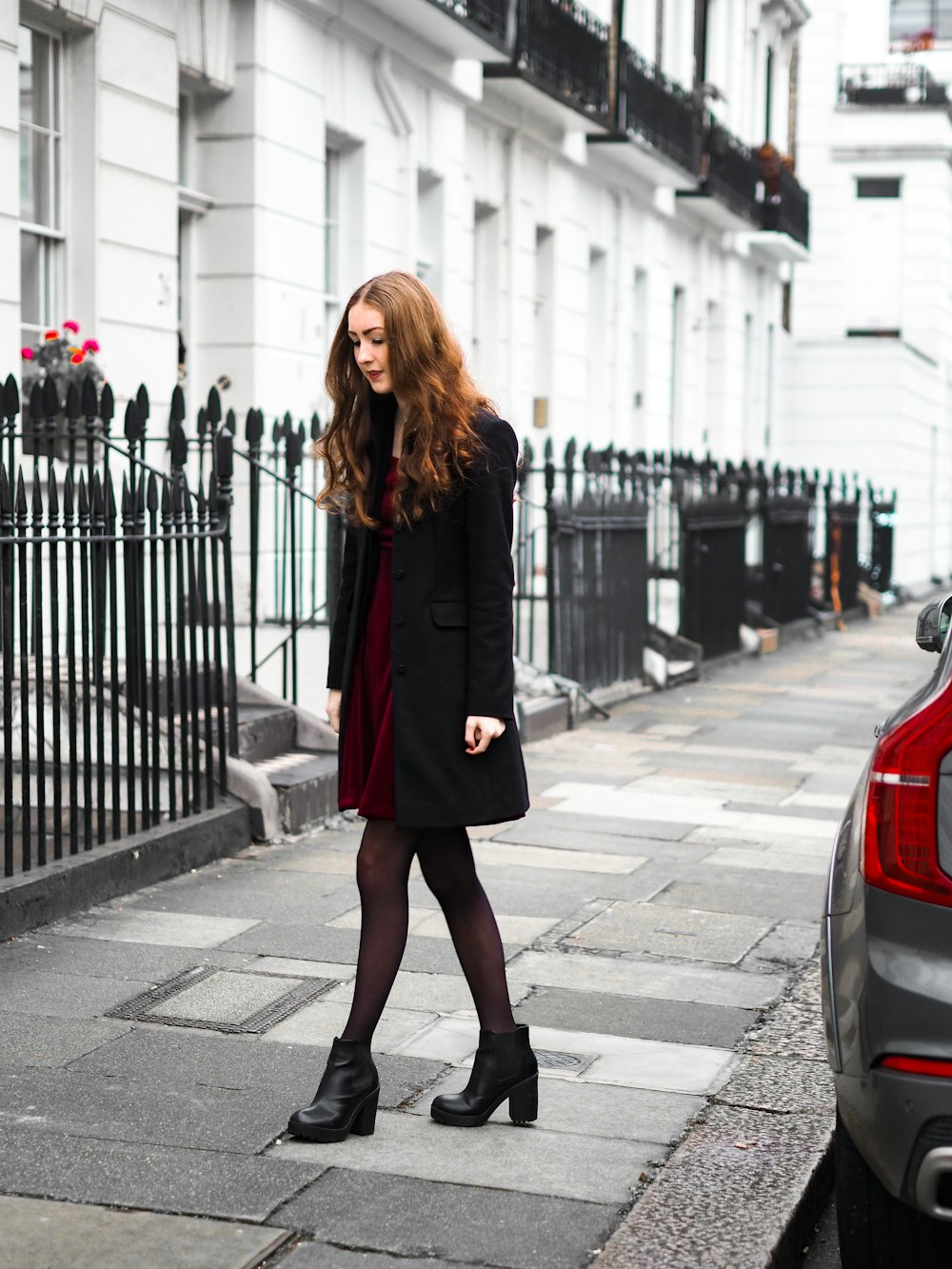 woman in black coat standing on sidewalk during daytime