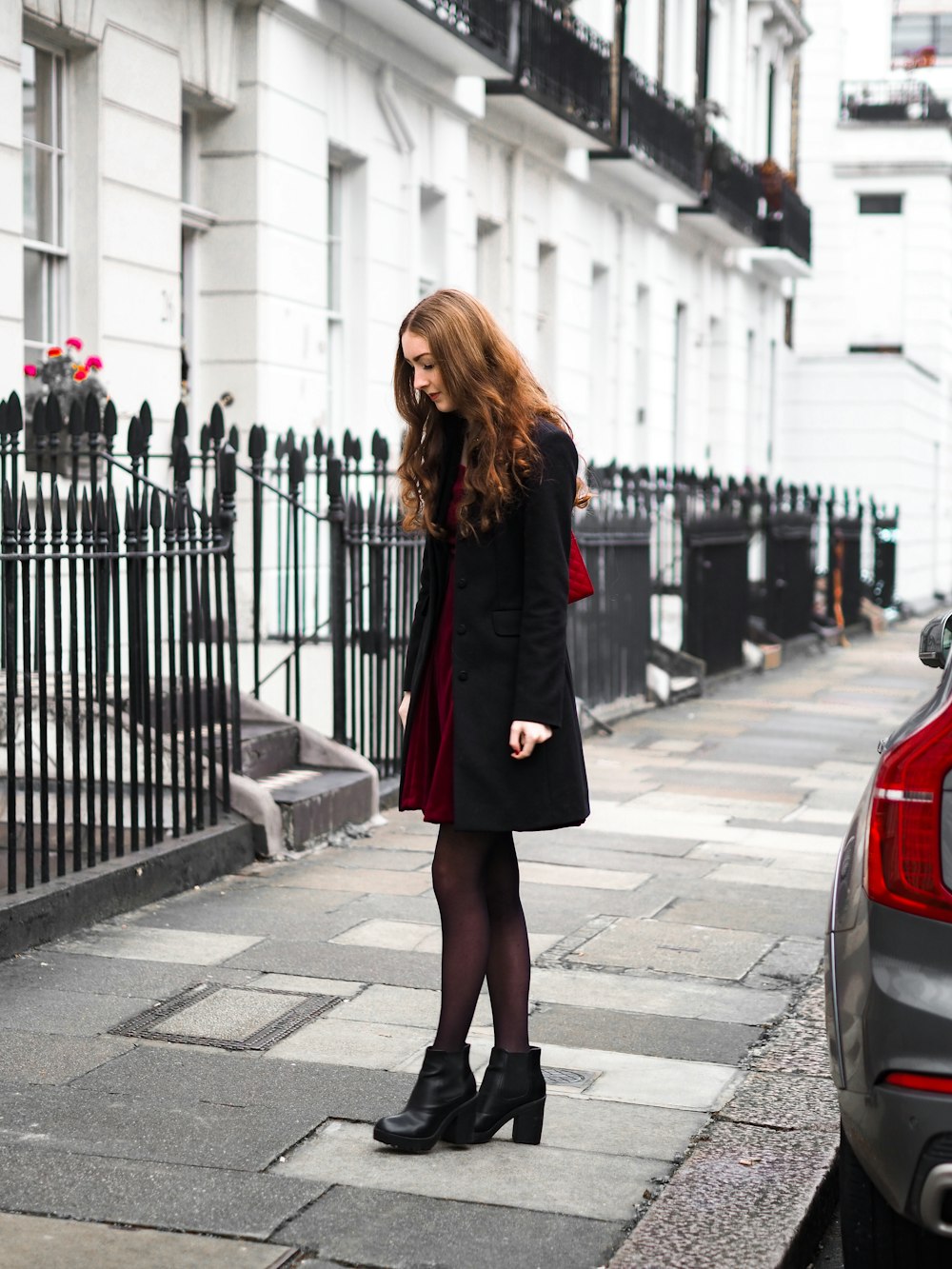 woman in black coat standing on sidewalk during daytime