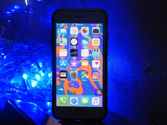 A smartphone with a colorful home screen is positioned upright against a dark backdrop. To the left, a cluster of bright blue LED lights casts an illuminating glow.