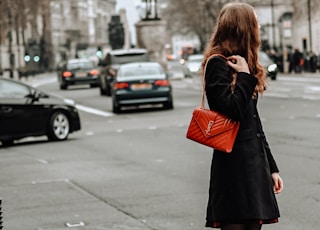 woman in black coat standing on sidewalk during daytime