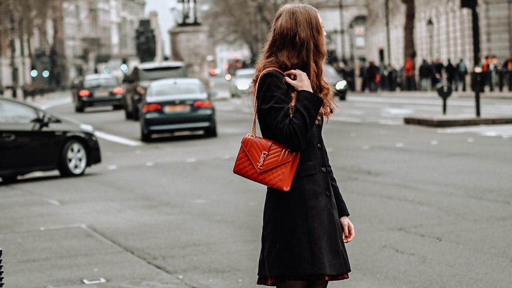 mujer camina por la calle y sostiene un bolso de marca en de color rojo en su hombro