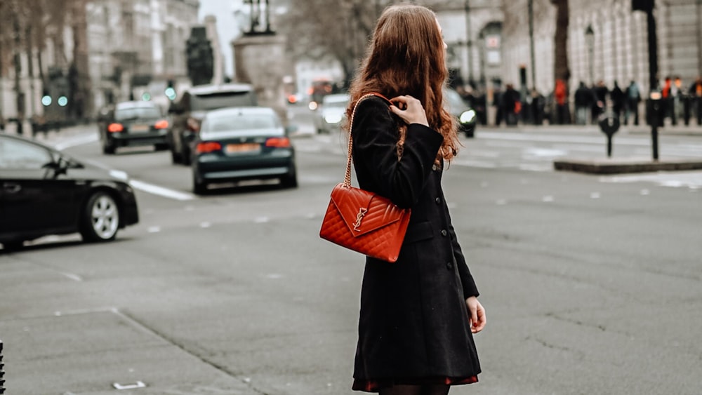 femme en manteau noir debout sur le trottoir pendant la journée