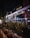 A nighttime scene of an Italian restaurant with a well-lit glass facade. The exterior includes decorative plants in rectangular planters lining the sidewalk. Soft interior and exterior lighting casts a warm glow, highlighting the restaurant signage.