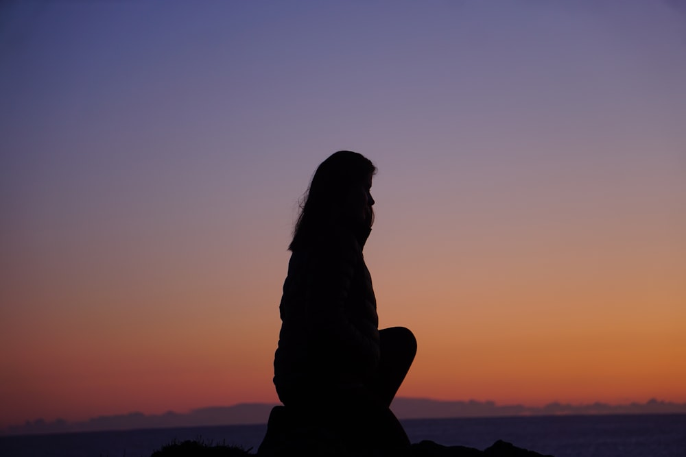 silhouette of woman sitting on rock during sunset